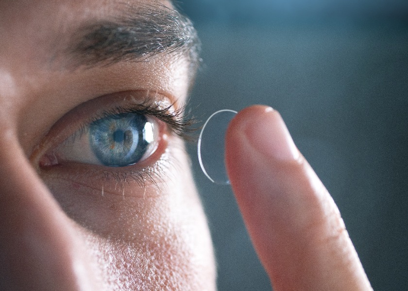 Close-up of a man putting contact lenses on blue eye. Concept of: healtcare, optic, hydration of the eye.