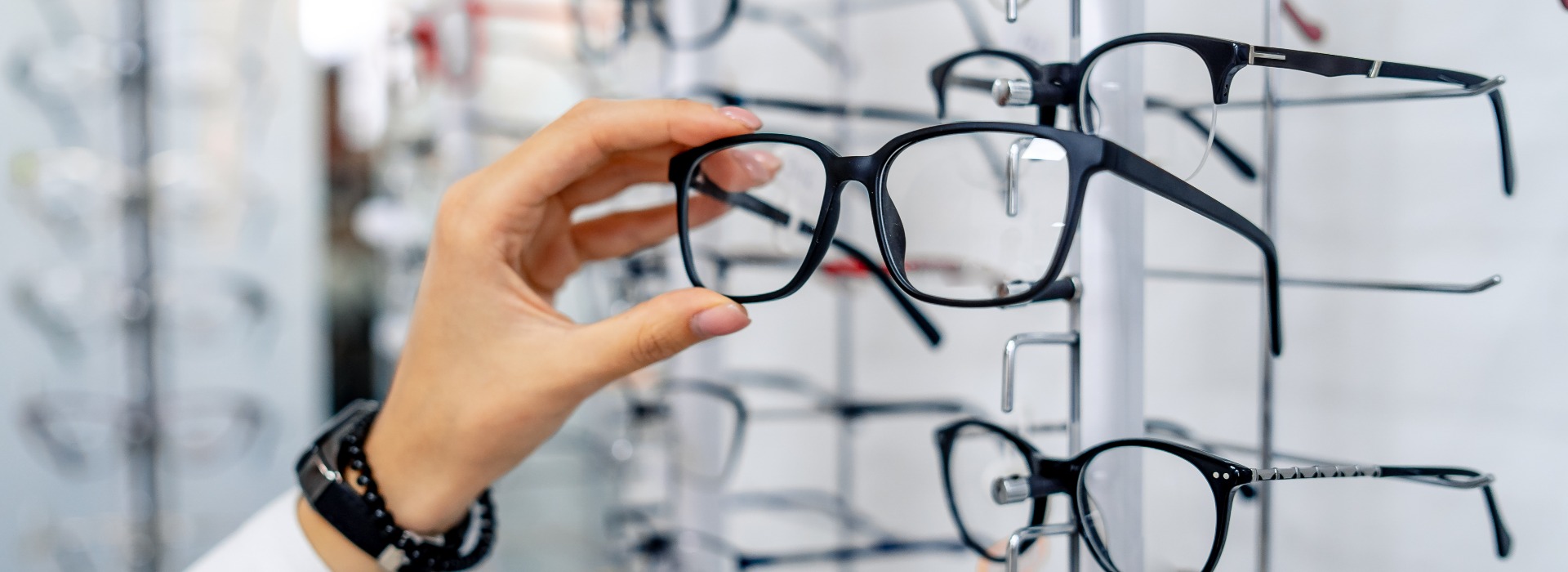 Row of glasses at an opticians. Eyeglasses shop. Stand with glasses in the store of optics. Woman chooses spectacles. Eyesight correction.